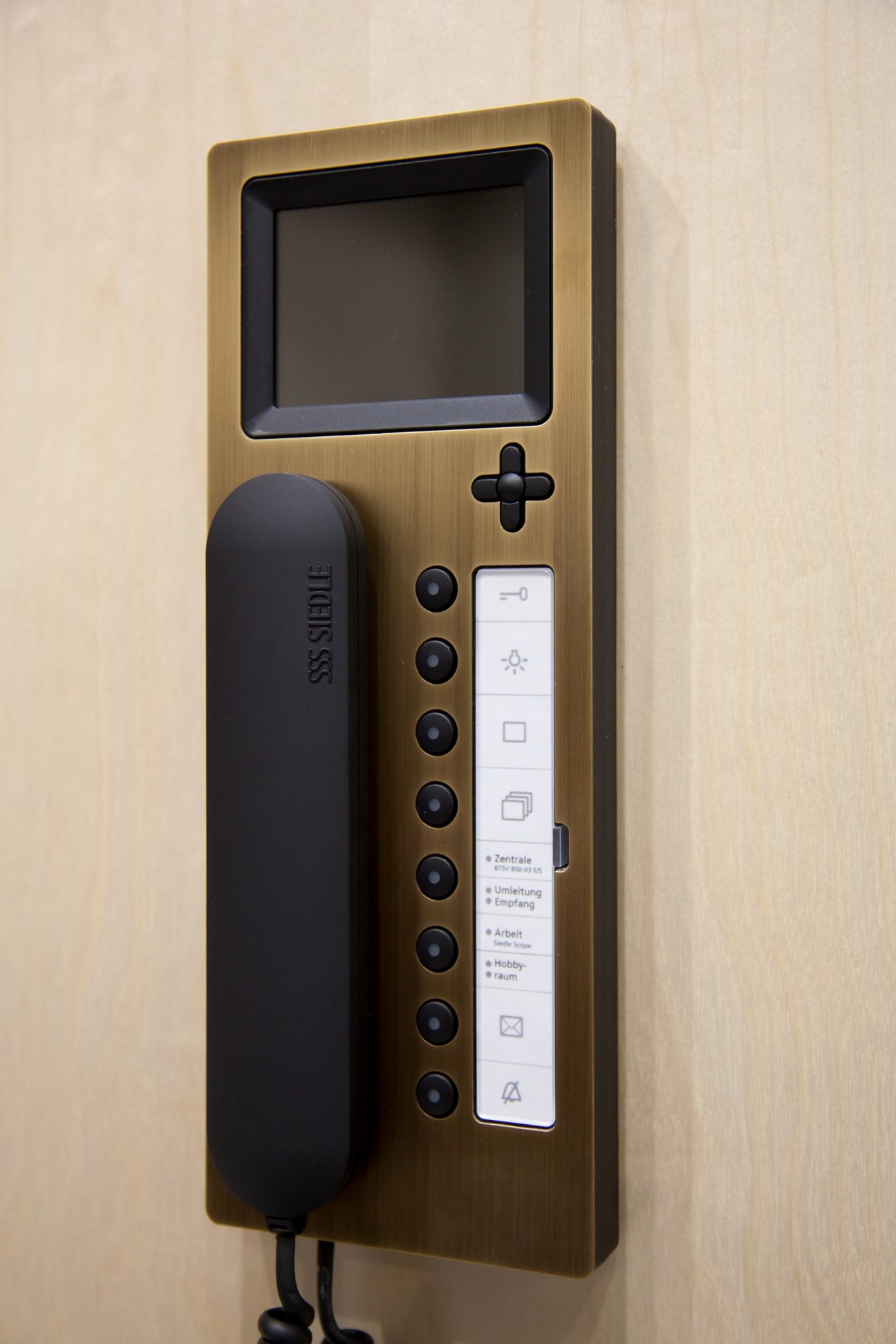 Siedle video intercom system with brass frame, display screen, handset and control buttons on wall.