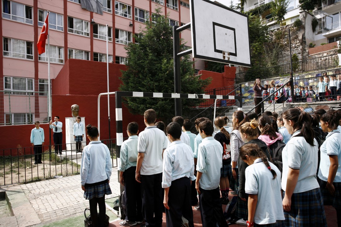 Students in school uniforms gather in a playground near a basketball hoop and Turkish flag at Cihangir primary school in Istanbul.