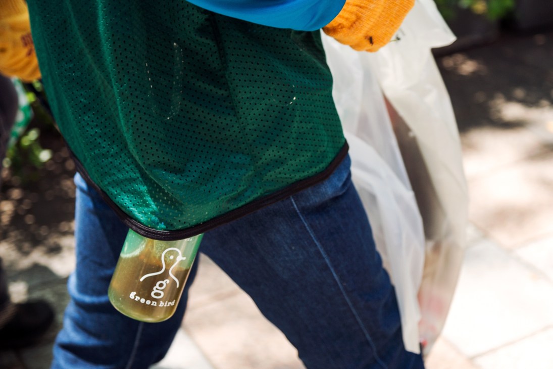 Close-up of a Green Bird volunteer wearing a green Nike mesh vest and holding a water bottle with the Green Bird logo.