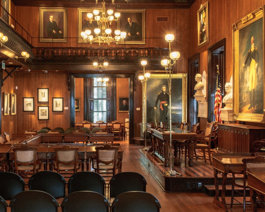 Interior of Charleston City Hall with wood paneling, portraits, chandelier, and period furniture.