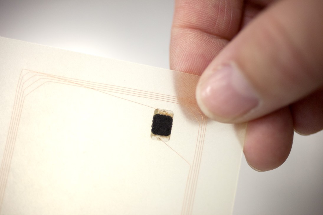 A tiny black NXP semiconductor chip held between fingertips over a document with line drawings.