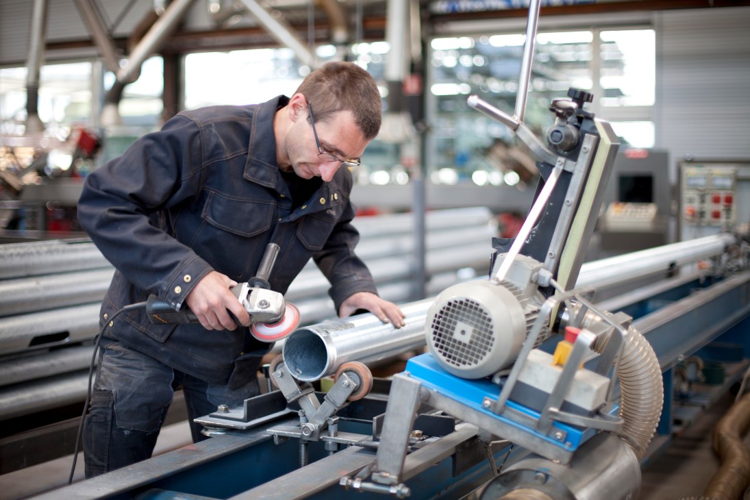 Factory worker using a power sander on a cylindrical lamp component at Ewo's facility.