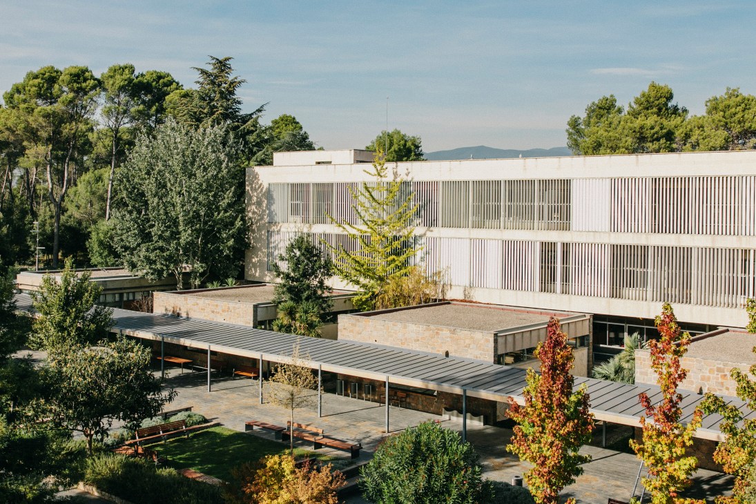 Exterior courtyard of Parc de Belloch, a modernist building with vertical ribbed facade and landscaped grounds featuring autumn foliage.