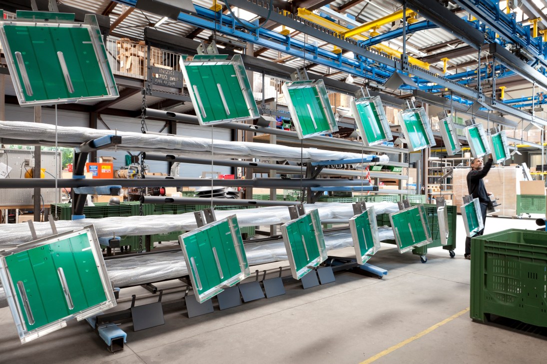 Green lamp shades hanging from metal poles on an assembly line at Ewo's factory in South Tyrol.