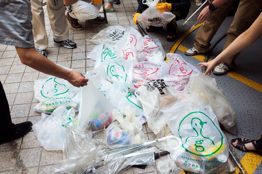 Green Bird volunteers sort collected rubbish into branded white bags with the green bird logo.
