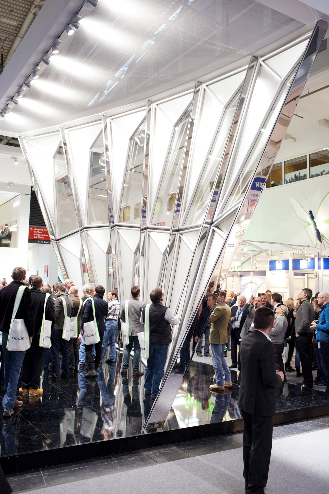 Visitors gather around Schüco's architectural façade display featuring large angled glass and metal panels at the BAU construction fair.
