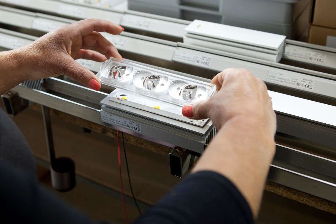 Hands installing LED modules into a white lamp fixture with visible components and wiring.