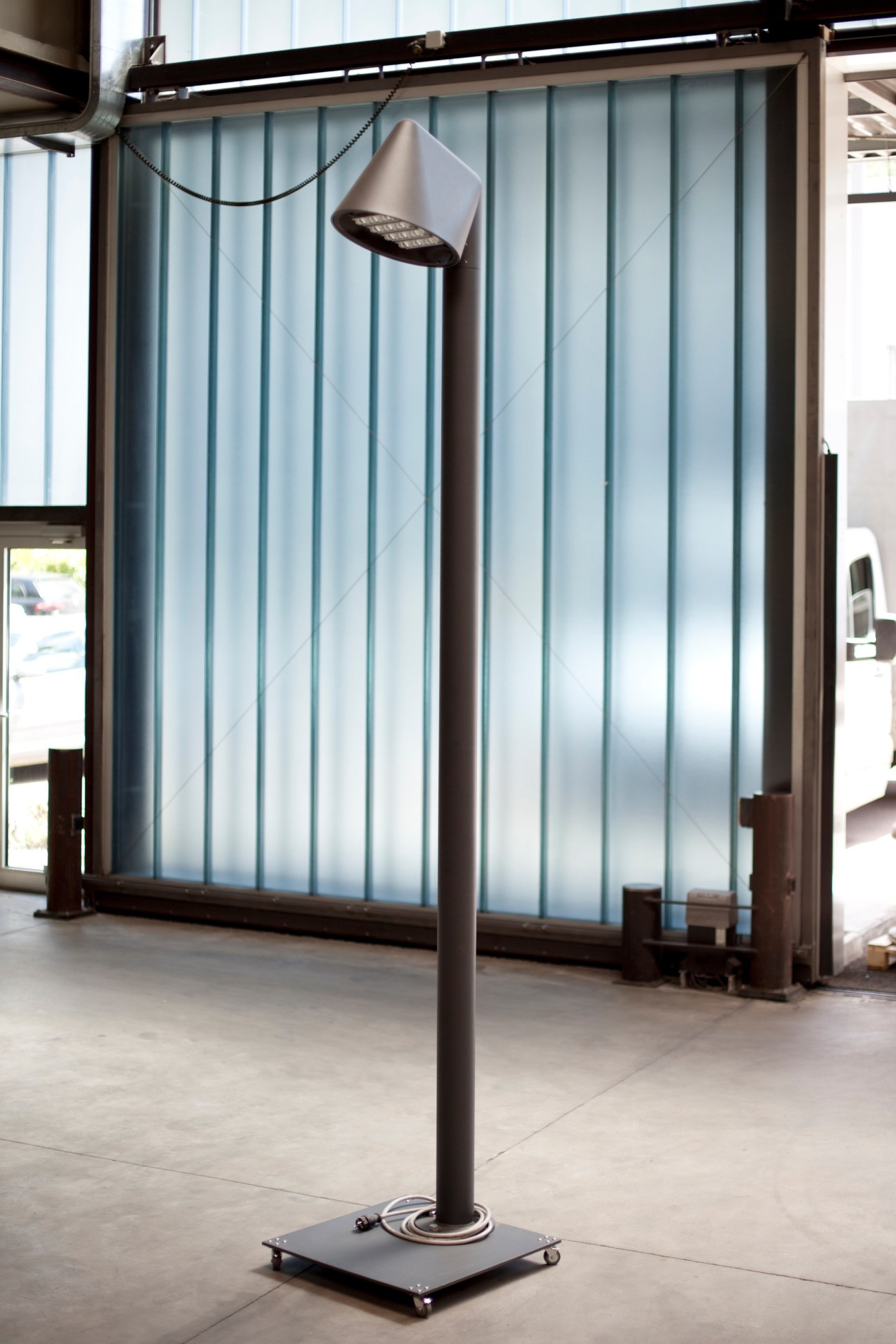 Ewo's LED UN Luminaire street lamp with geometric cone-shaped head on dark steel pole in modern showroom