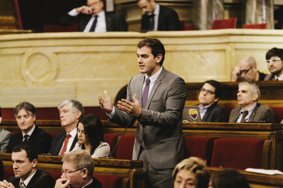 Albert Rivera speaking in the Catalonian parliament chamber, wearing a gray suit and purple tie.