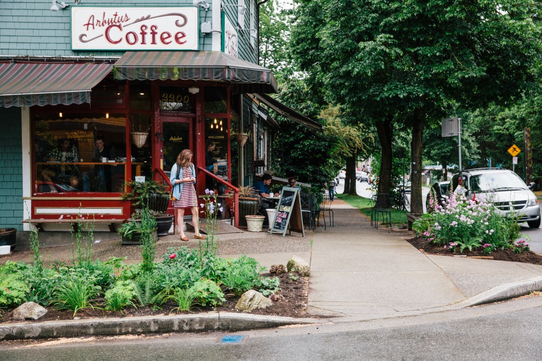 Arbutus Coffee storefront with planted garden beds featuring flowers and greenery along the sidewalk.