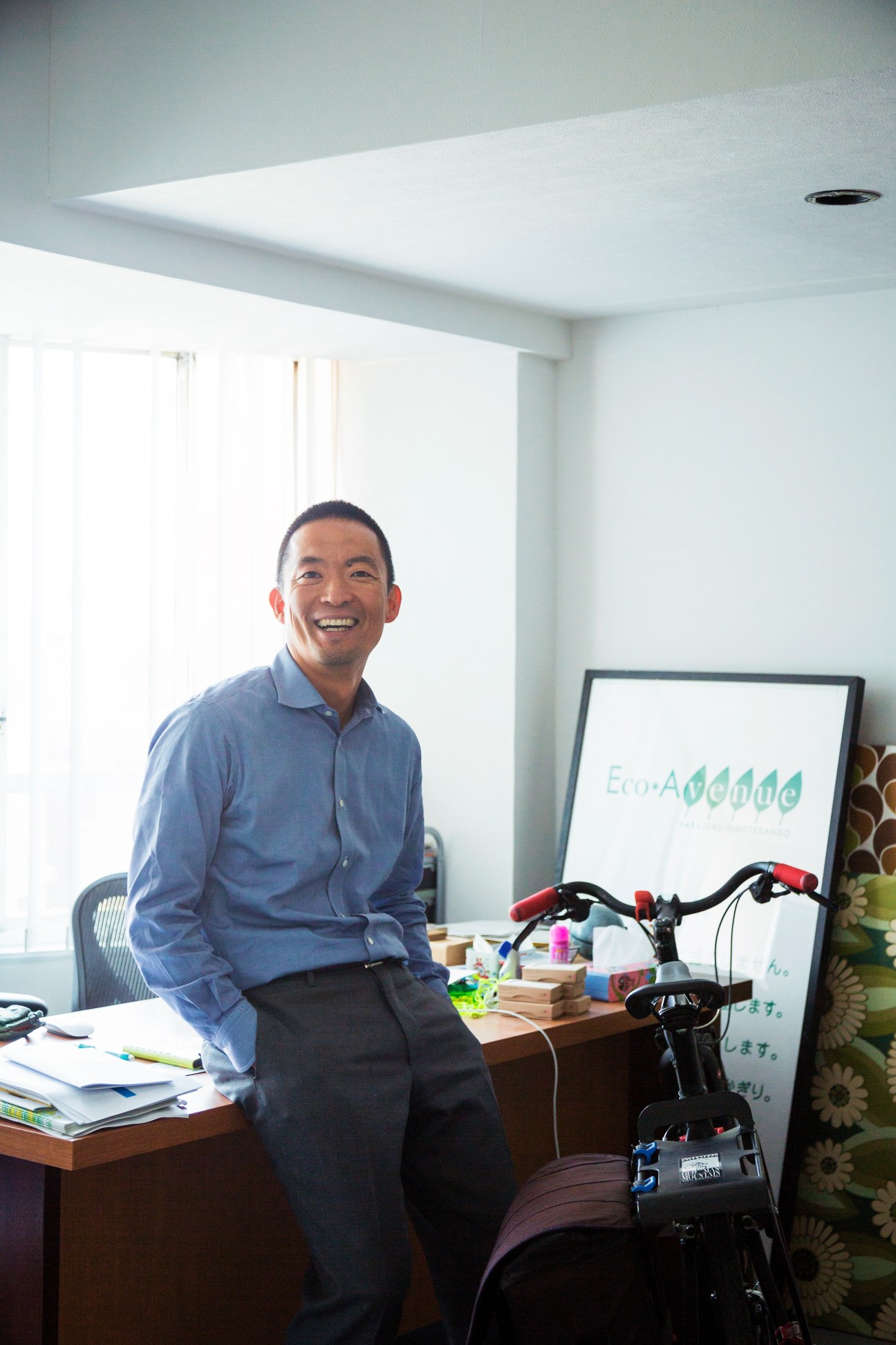 Ken Hasebe, founder and chairman of Green Bird, smiling in his office with a bicycle nearby.