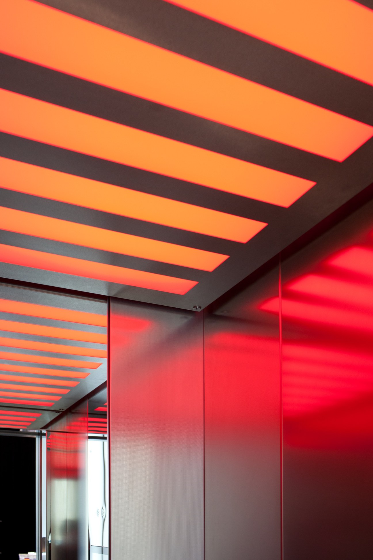 Modern interior with illuminated orange ceiling panels and red-lit glass sliding door.