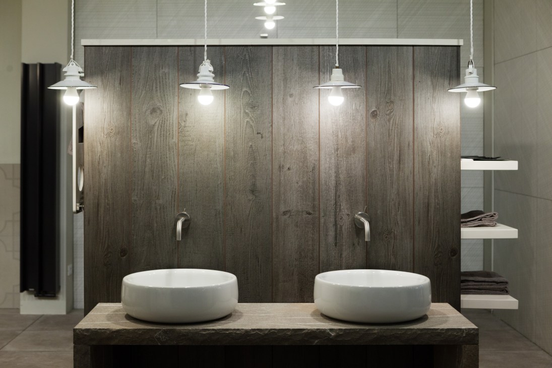 Modern bathroom with dual round white sinks, wood-grain wall panels, and pendant lighting