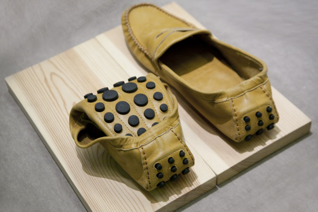 Pair of tan leather folding driving slippers with black stud details displayed on light wood.