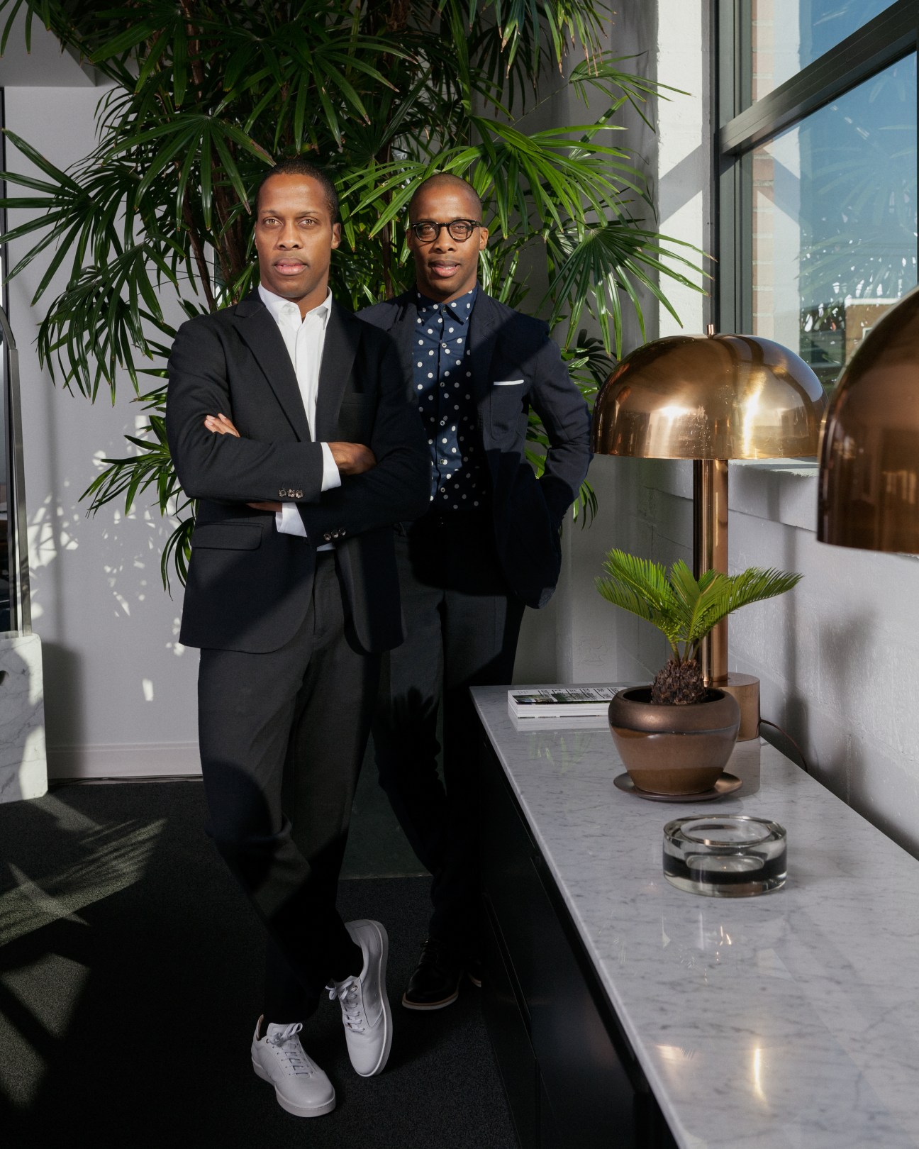 Byron and Dexter Peart, co-founders of Want les Essentiels de la Vie, posing in a modern office with plants and brass lighting.