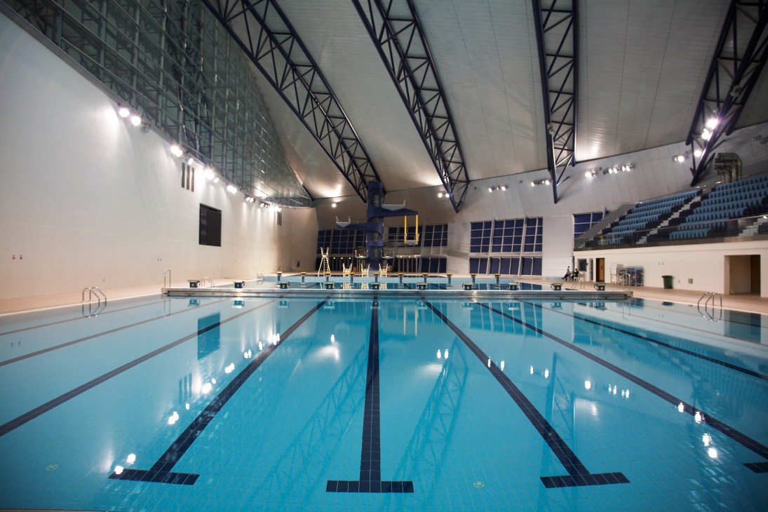 Empty indoor Olympic-sized swimming pool with lane dividers under bright stadium lighting.