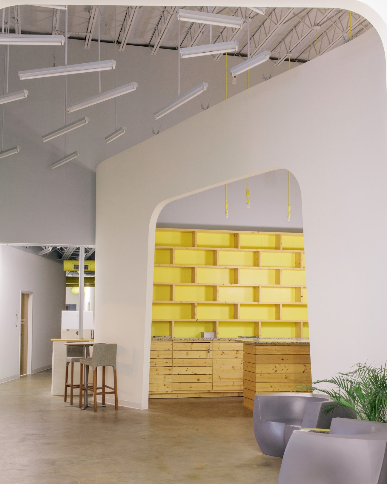 Modern office interior with yellow storage shelving, industrial lighting, and contemporary seating.