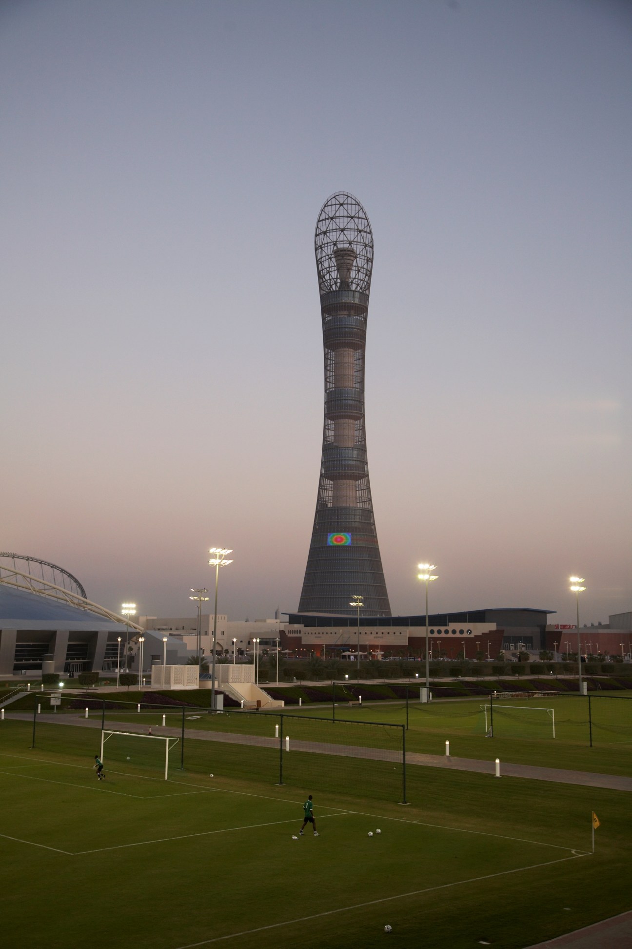 Aspire's football pitches with the distinctive Torch Tower structure illuminated at dusk in Doha, Qatar.