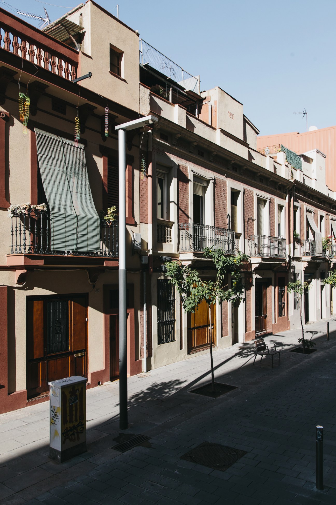 A street in Poblenou with historic brick and terracotta buildings featuring wooden doors and wrought iron balconies.
