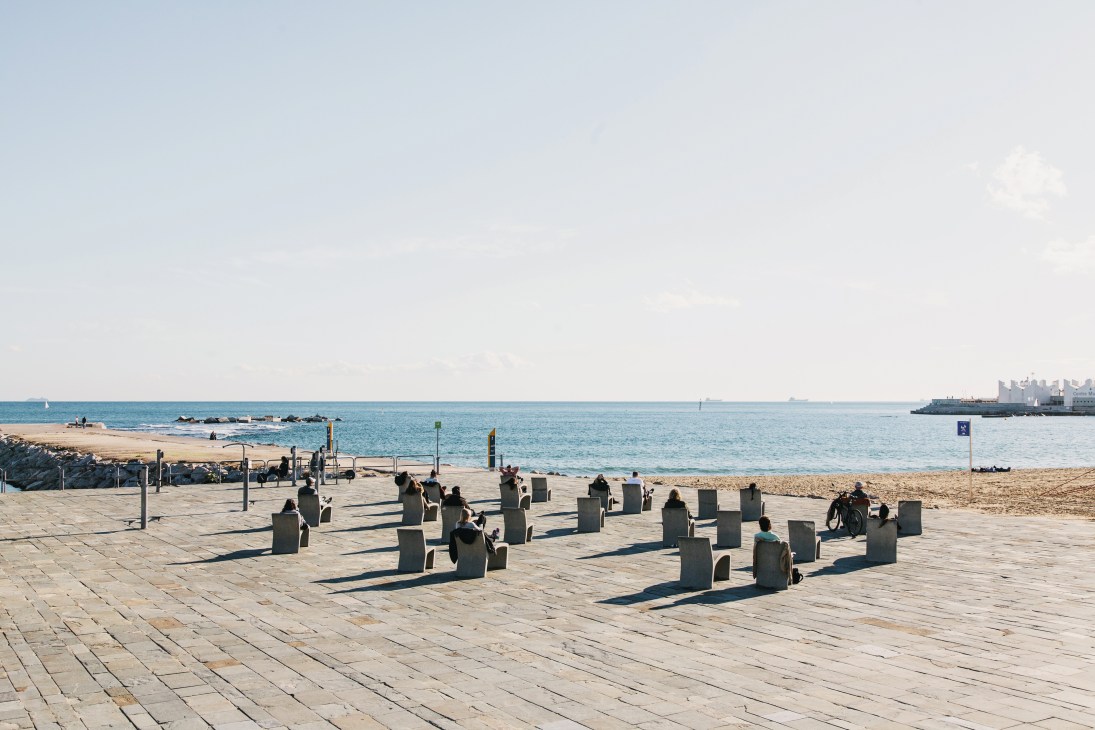 People relaxing on Bogatell Beach boardwalk with sea and beach in background.