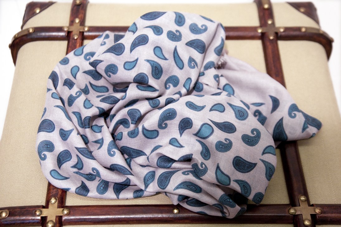 Paisley scarf from Begg in blue and white tones arranged on a vintage leather suitcase.