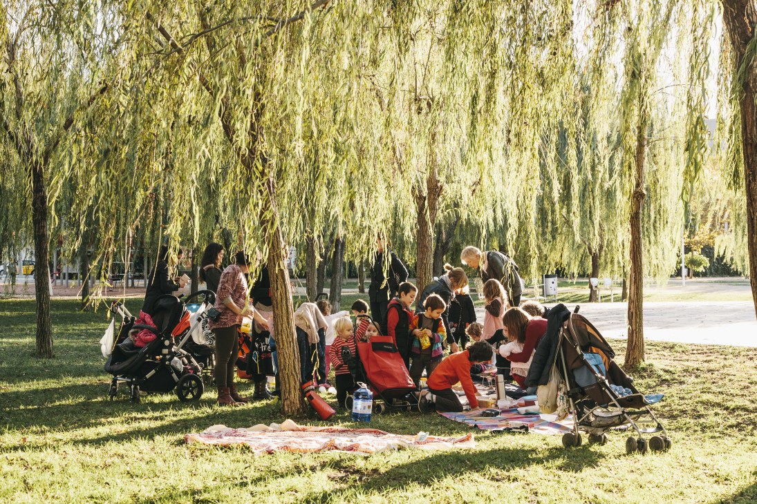 Families with children picnicking under weeping willow trees in Parc del Centre del Poblenou, Barcelona.