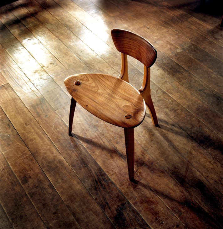 Wooden chair with curved back and seat on wooden floor in sunlight.