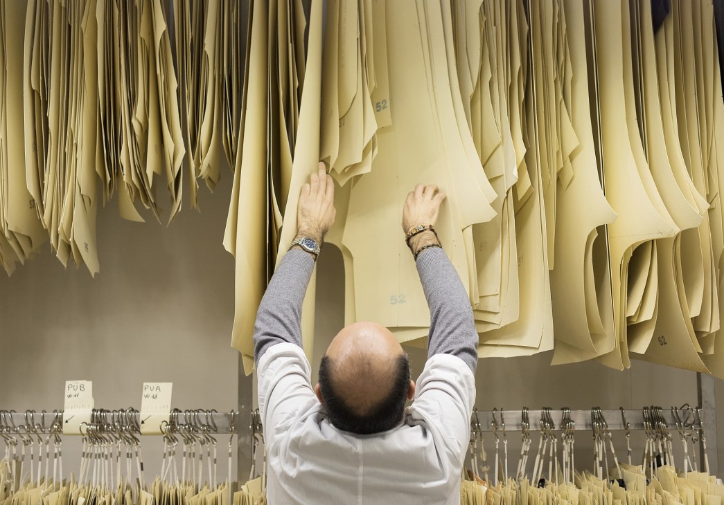 A tailor examines hanging fabric patterns at Cesare Attolini tailoring workshop.