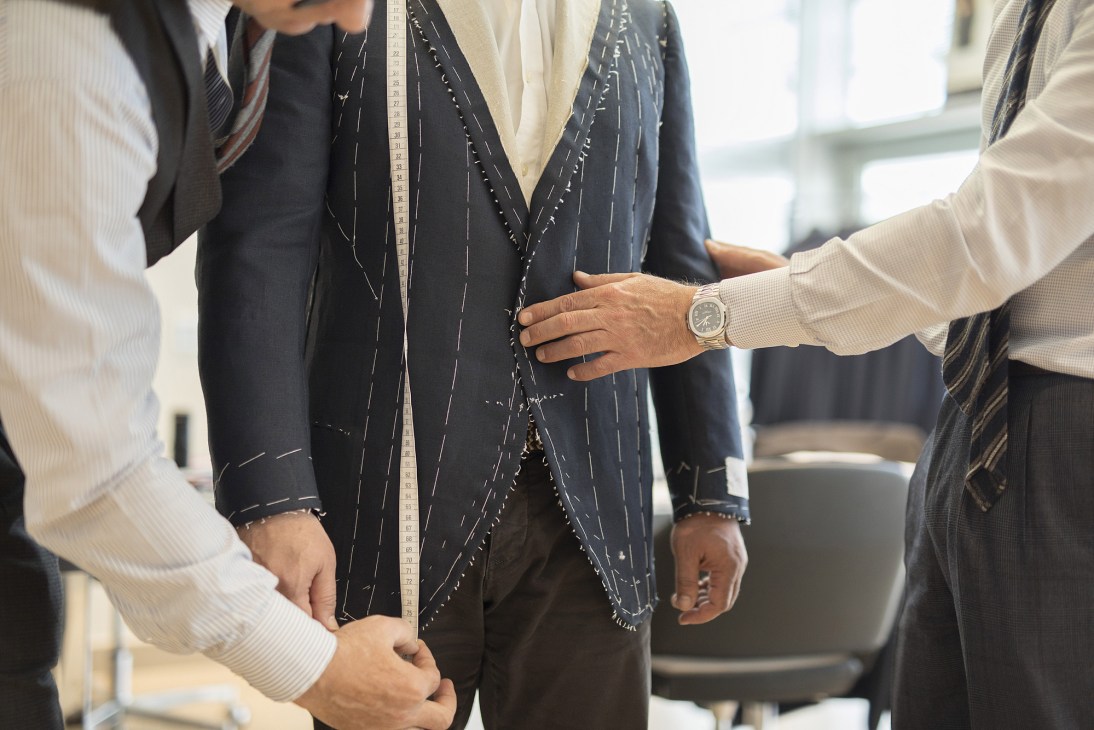 Tailors fitting a dark pinstriped suit on a client at Cesare Attolini atelier.