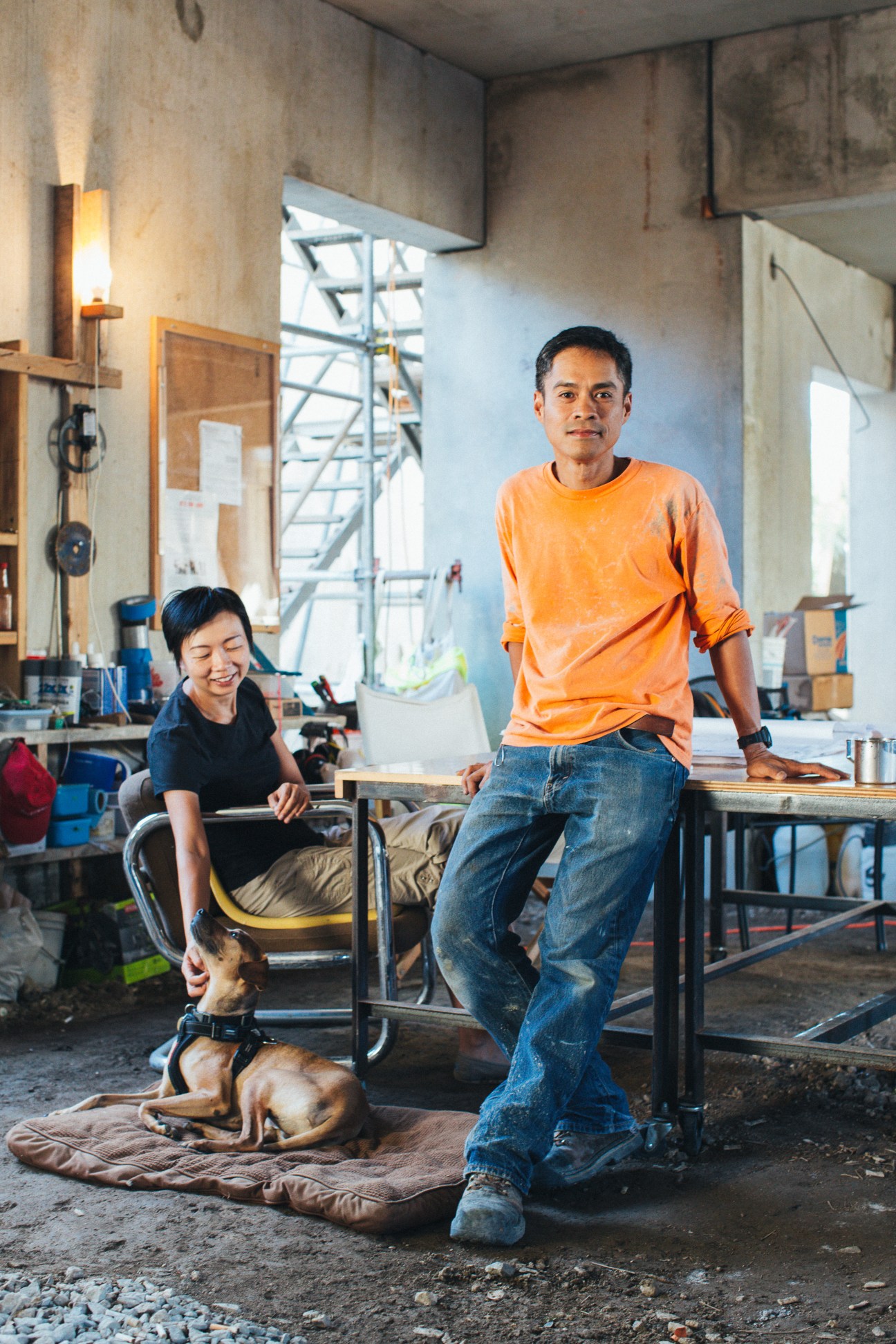 Janice Li and Bundit Kanisthakhon sitting in their concrete workshop with tools and a dog
