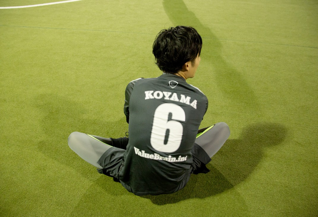 Young player in black futsal jersey with "KOYAMA 6" stretching on green indoor court