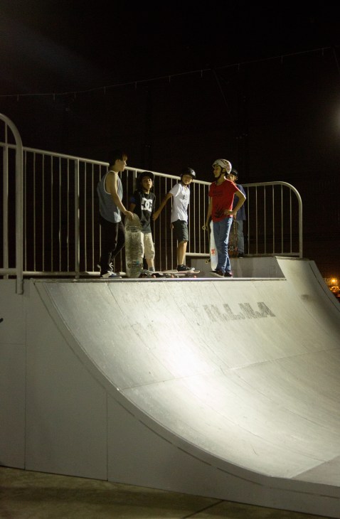 Five young people standing on a skateboard ramp at night, preparing to ride.