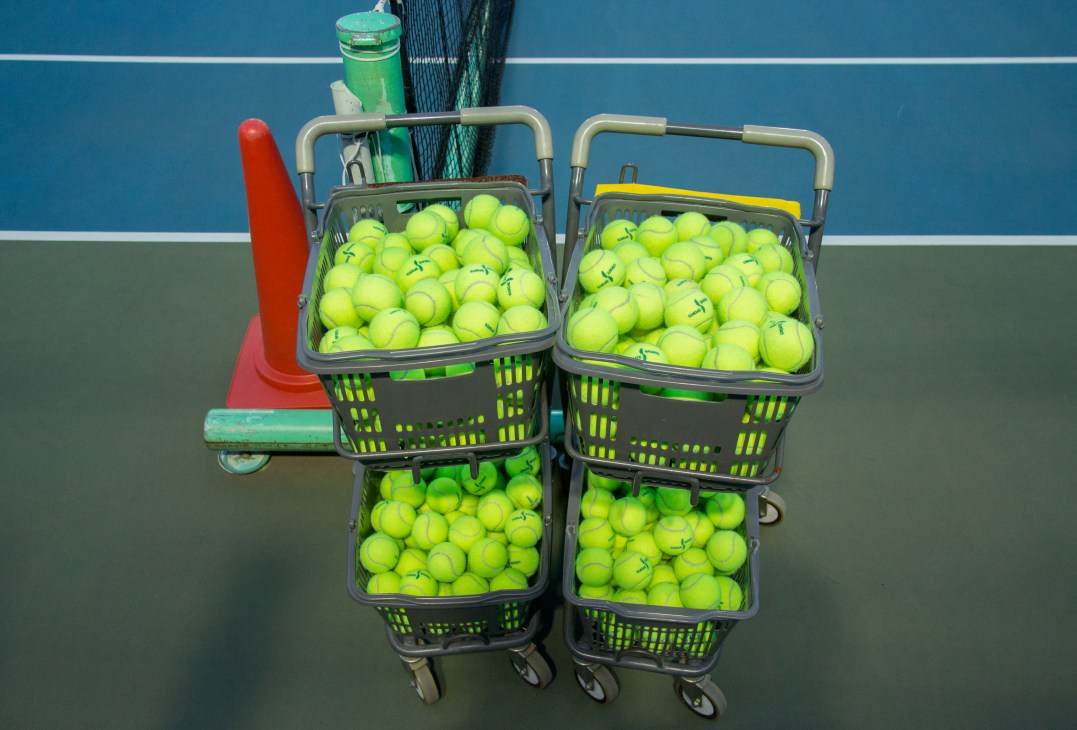 Tennis ball collection baskets filled with fluorescent yellow balls stacked on a rooftop court.