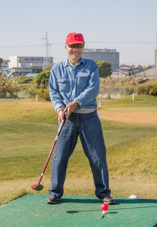 Senior man in red cap and blue shirt playing mini golf on outdoor course