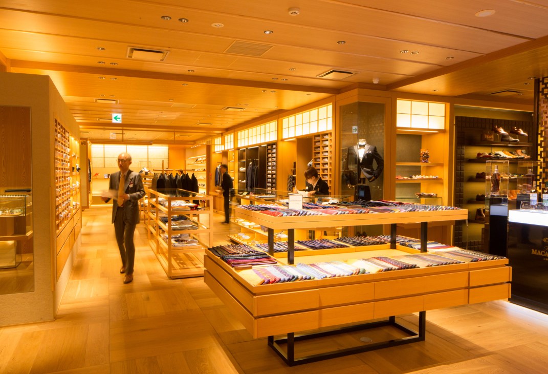 Interior of Isetan Mitsukoshi luxury department store with warm wood tones, display tables, and shoppers browsing apparel.