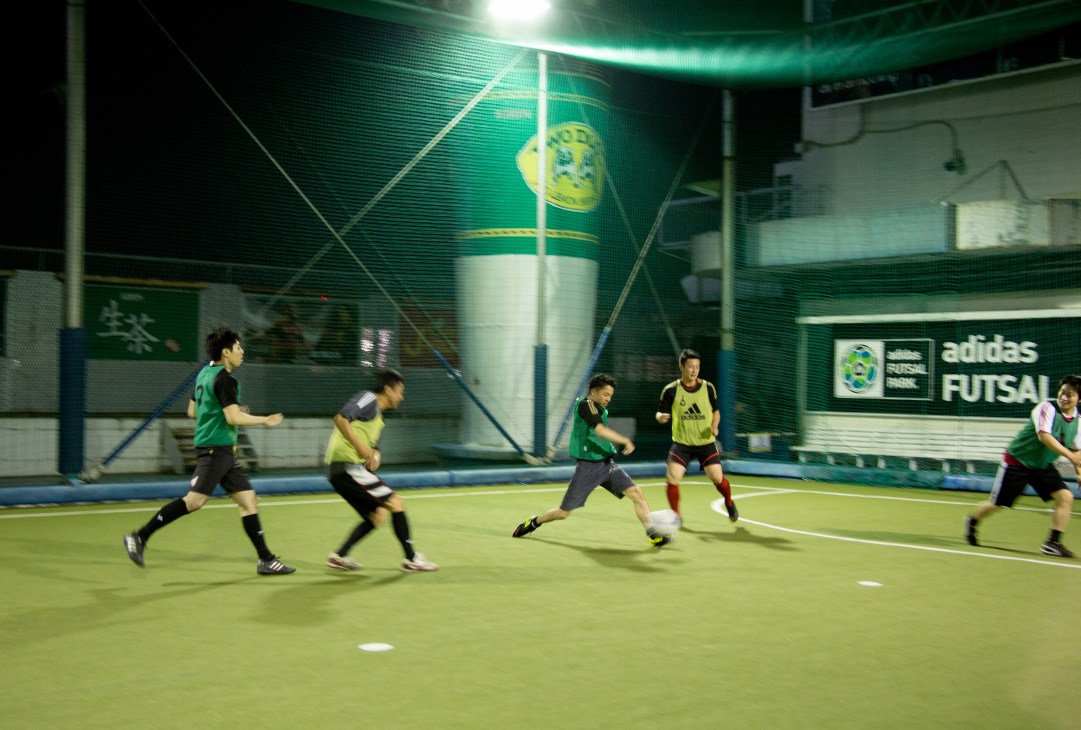 Players in green and yellow uniforms playing futsal on an indoor court with Adidas branding visible