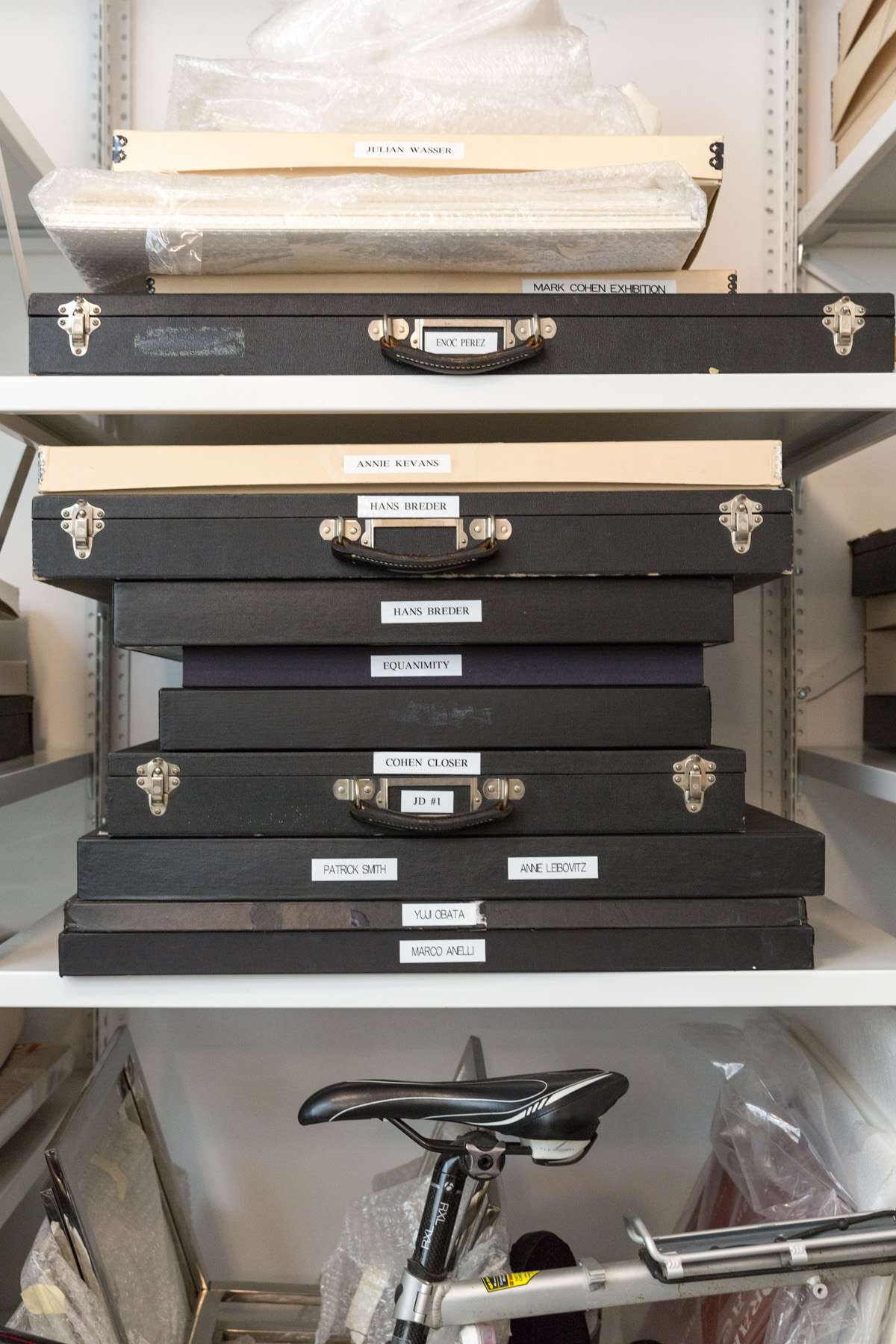 Stacked black and cream artist portfolios with gold-embossed labels on a white shelf.