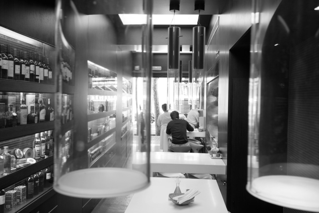 Interior of Semon restaurant in Barcelona showing counter seating, pendant lighting, and display shelves with products.