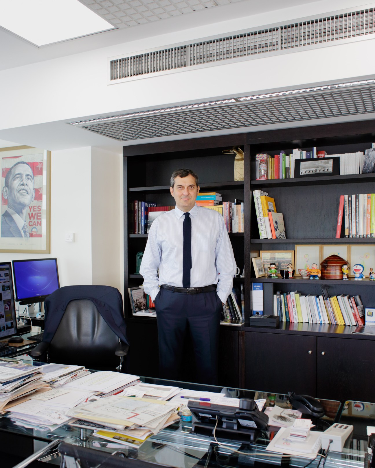 Mario Calabresi, editor in chief of La Repubblica, stands in his office with bookshelves and desk covered with newspaper layouts.