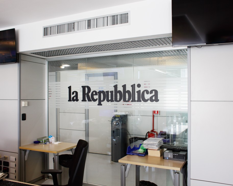 Glass-walled office space with 'la Repubblica' logo and desks inside a modern newsroom.