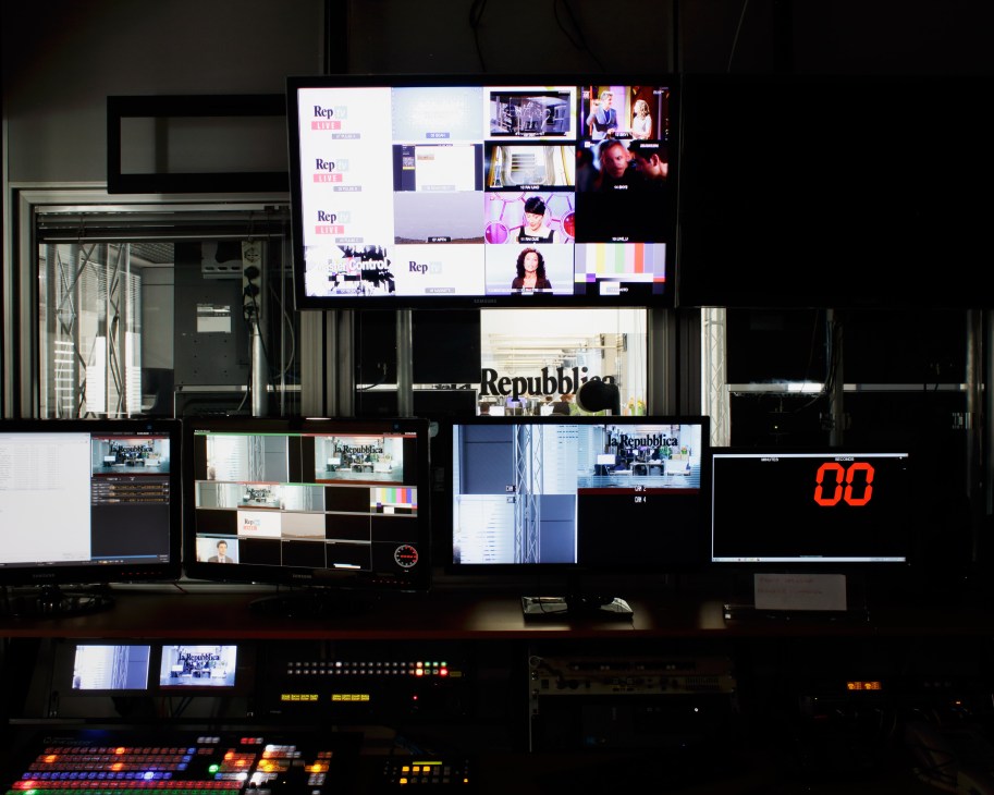 Control room with multiple monitors displaying La Repubblica branding and video feeds from news production.