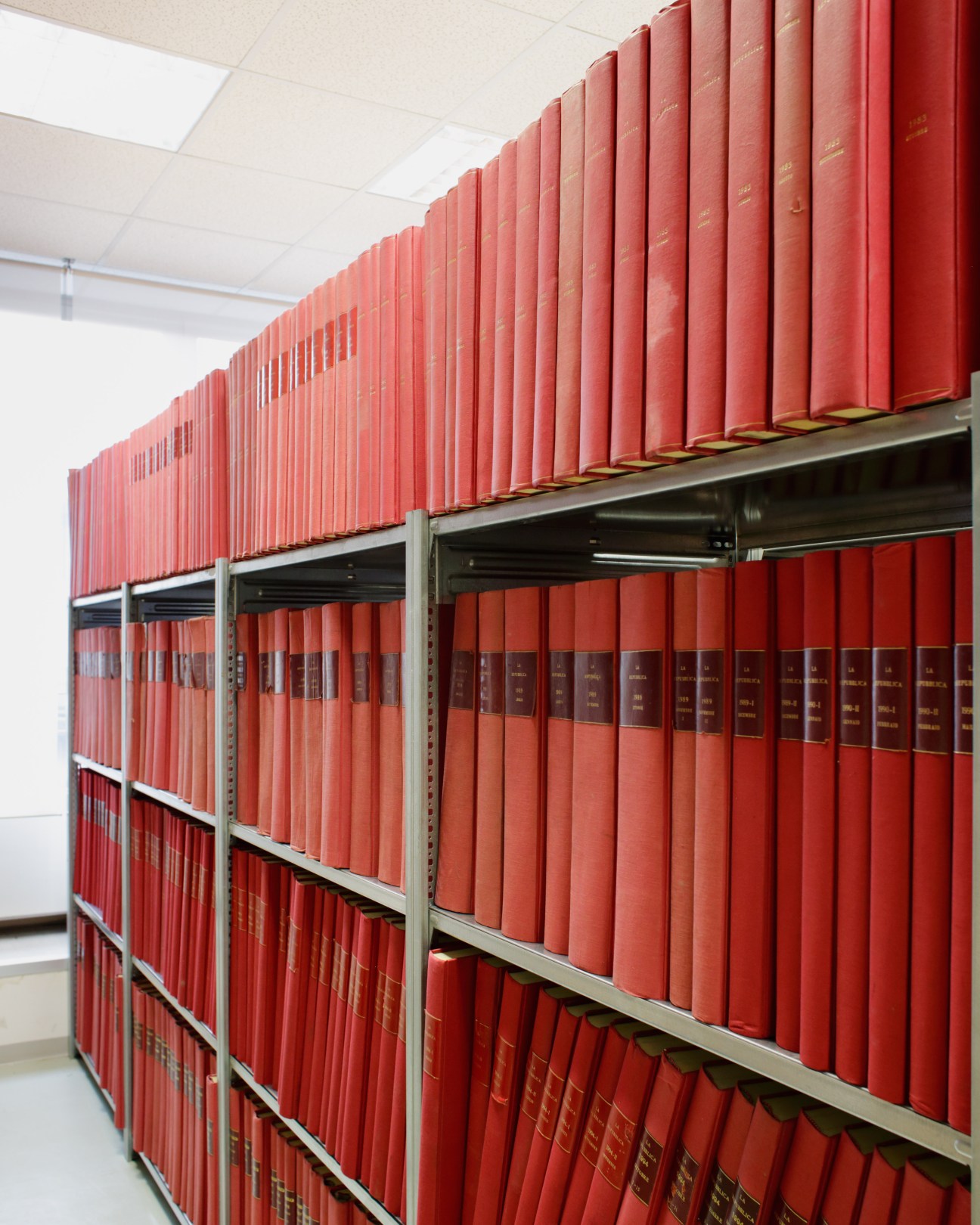 Metal shelving unit filled with red bound volumes of archived La Repubblica newspaper editions.