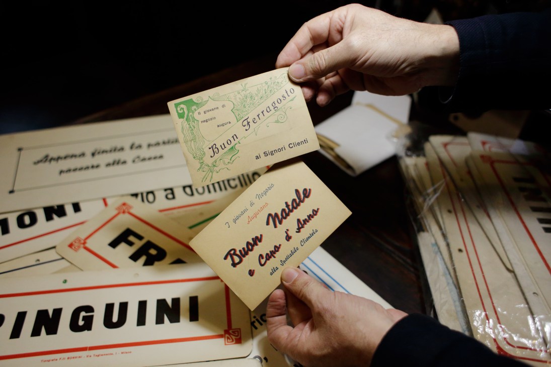 Hand holding vintage Italian greeting cards and postcards with decorative text and illustrations from the early 20th century.