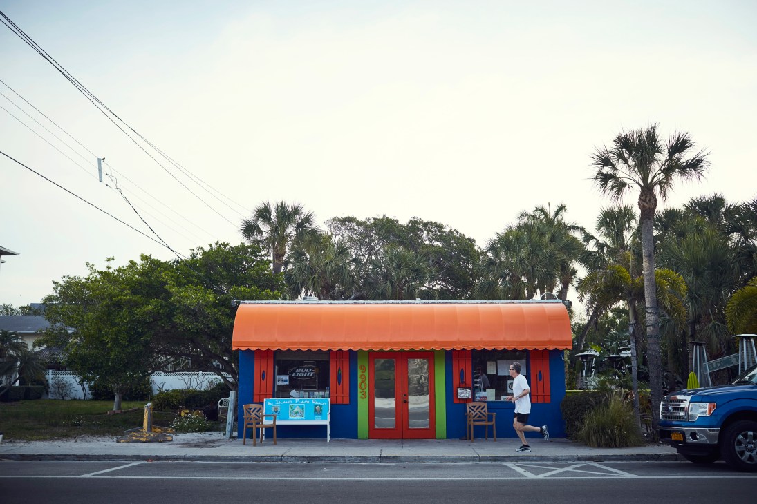 Colorful beachside bar and grill with bright orange roof, blue and red walls, and palm trees on Anna Maria Island, Florida.