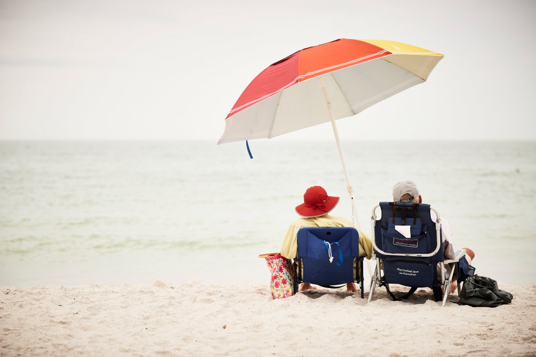 Two people sitting on beach chairs under a colorful umbrella facing the ocean.