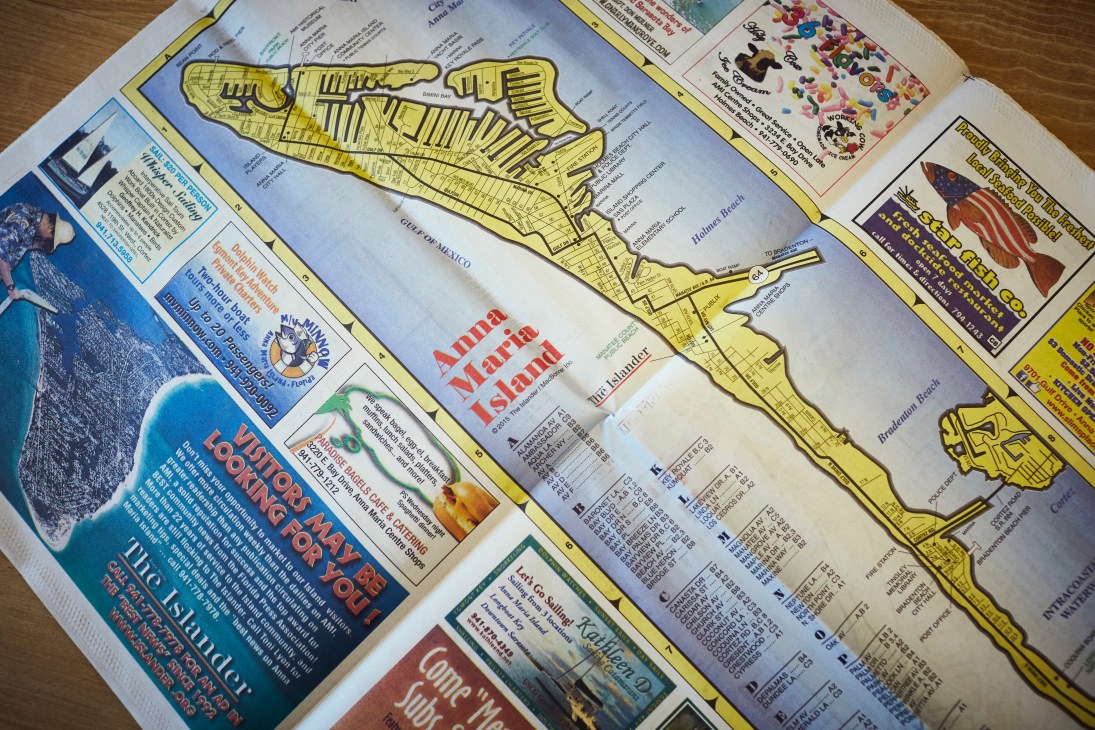 Map of Anna Maria Island showing its three cities with yellow highlighted streets and surrounding water, displayed alongside The Islander newspaper.