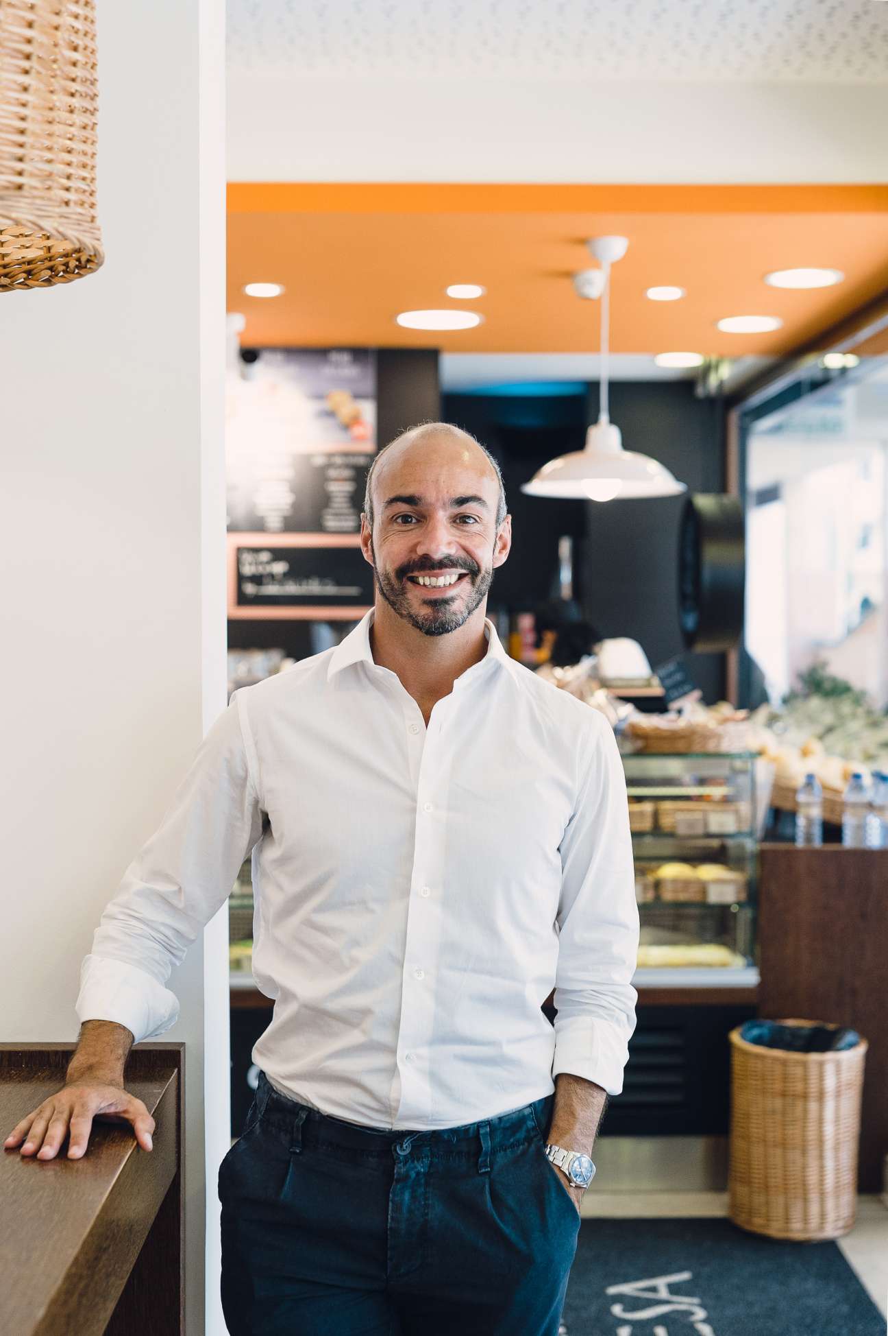 Nuno Carvalho, founder and CEO of A Padaria Portuguesa, stands smiling in one of his café-bakery shops with an orange ceiling and modern design.