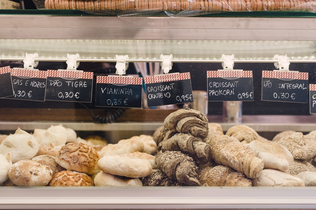 A Padaria Portuguesa bakery display case with fresh pastries, breads and croissants behind glass with Portuguese price labels.