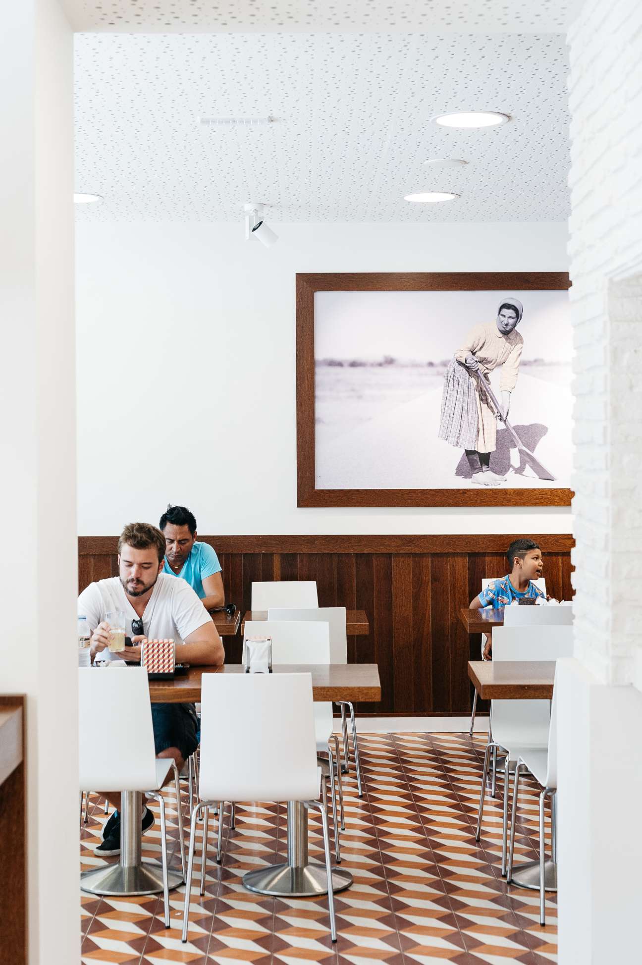 Interior of A Padaria Portuguesa café with customers seated at tables and vintage photograph on wall.