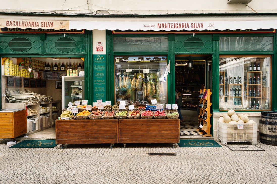Manteigaria Silva storefront in Lisbon with green doors, hanging cured meats, and produce display, established 1890.